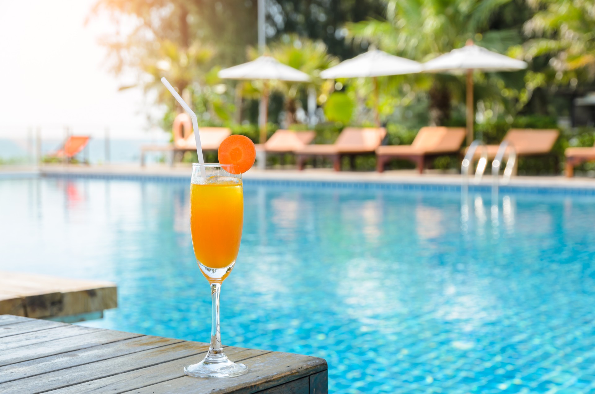 Orange juice glass on wooden table with swimming pool view background